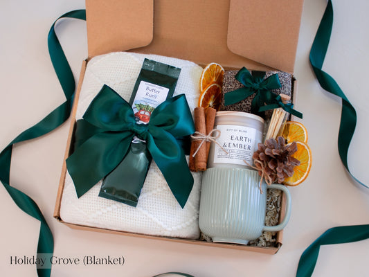 Rustic green holiday gift box for him featuring a ribbed ceramic mug, Earth & Ember candle, butter rum coffee, cinnamon sticks, dried orange slices, pinecone, and a soft white blanket - finished with deep green ribbons for a cozy, nature-inspired winter aesthetic.