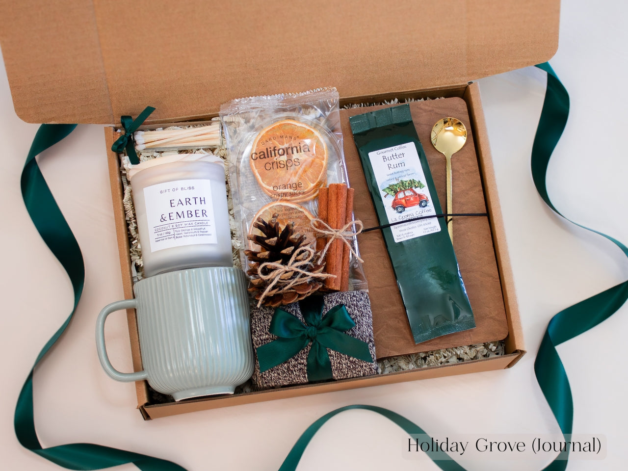 Spruce-green Christmas gift box for him with ribbed ceramic mug, Earth & Ember candle, butter rum coffee, dried oranges, pinecone, cinnamon sticks, journal, and gold spoon - an earthy and comforting holiday gift set tied with forest-green ribbon.