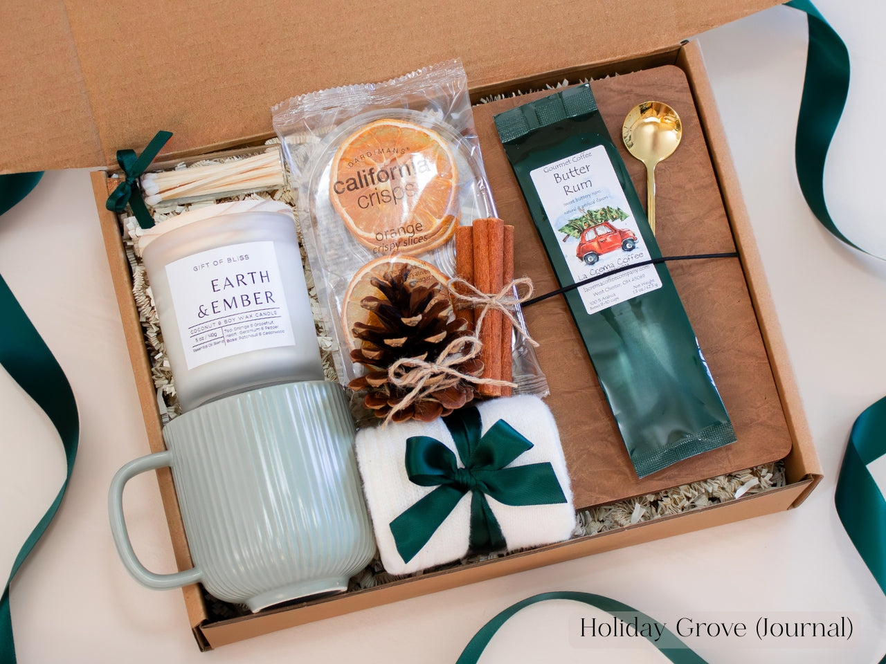Spruce-green Christmas gift box for him with ribbed ceramic mug, Earth & Ember candle, butter rum coffee, dried oranges, pinecone, cinnamon sticks, journal, and gold spoon - an earthy and comforting holiday gift set tied with forest-green ribbon.