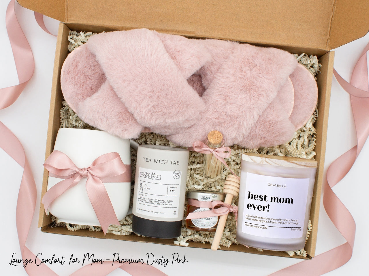 Gift box in a premium teal blue theme featuring cozy teal blue slippers, a minimalist ceramic mug tied with a teal blue ribbon, Winter Bliss tea, a glass jar of honey with a wooden dipper, a white-tipped match jar, and a mother-themed labeled aromatherapy candle in a frosted jar. All items are nestled in ivory crinkle paper and elegantly arranged for a luxurious and thoughtful gift for moms.