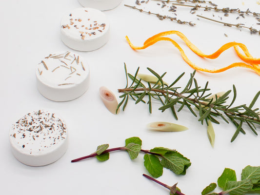 Three aromatherapy shower steamers are shown.  The first, 'Woodland Awakening', features lemongrass and cedar essential oils. The second, 'Revitalizing Breeze', features rosemary and eucalyptus. The third, 'Minty Mountains', contains mint essential oil.