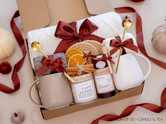 Couples’ gift box with calming tea, pure honey, wooden dipper, aromatherapy Earth & Ember candle, artisan safety match jar, 2 minimalist mugs, 2 long golden spoons, 2 pairs of cozy socks, soft white blanket, 2 cotton yarn coasters, dried orange slices and cinnamon sticks, all decorated with satin ribbon in fall color, neatly arranged in a kraft gift box — designed for peaceful evenings together.