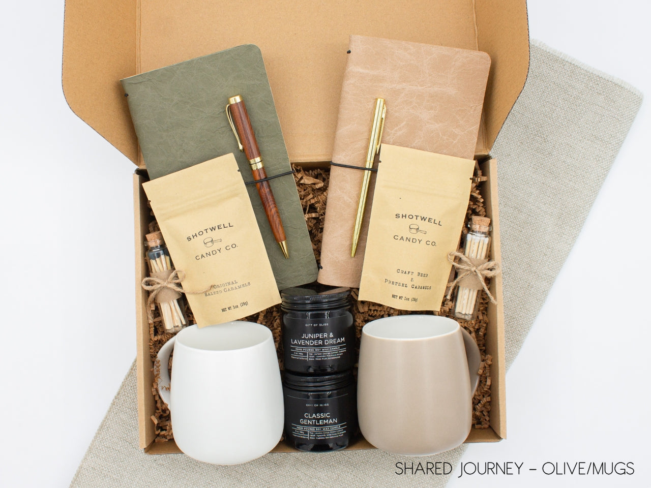 A gift box for two, features two ceramic mugs, two notebooks with a gold pen and a wooden pen, gourmet caramel candies, and two aromatic candles. Perfect for couples, friends, or colleagues to enjoy a relaxing, creative experience together.