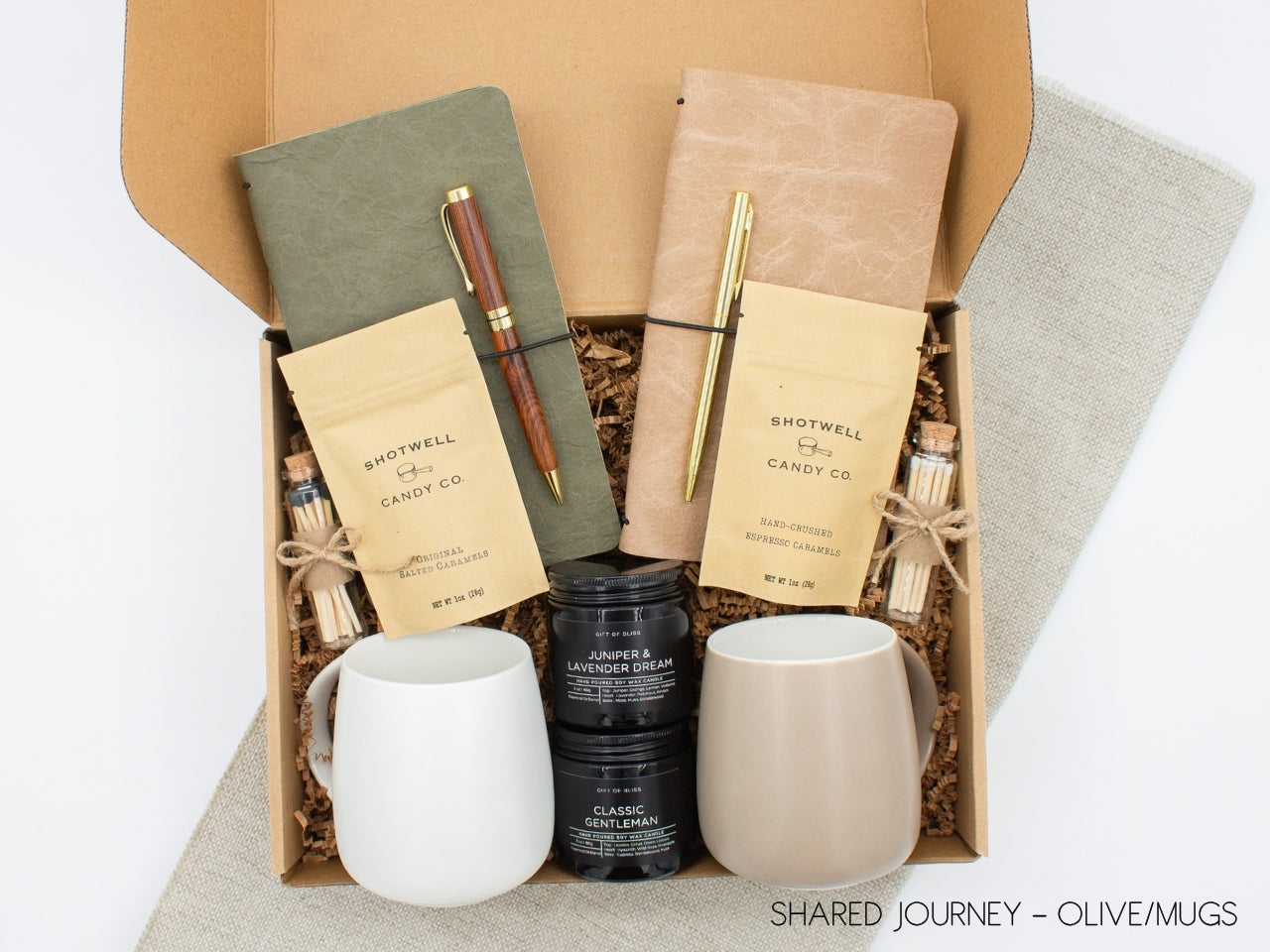 A gift box for two, features two ceramic mugs, two notebooks with a gold pen and a wooden pen, gourmet caramel candies, and two aromatic candles. Perfect for couples, friends, or colleagues to enjoy a relaxing, creative experience together.