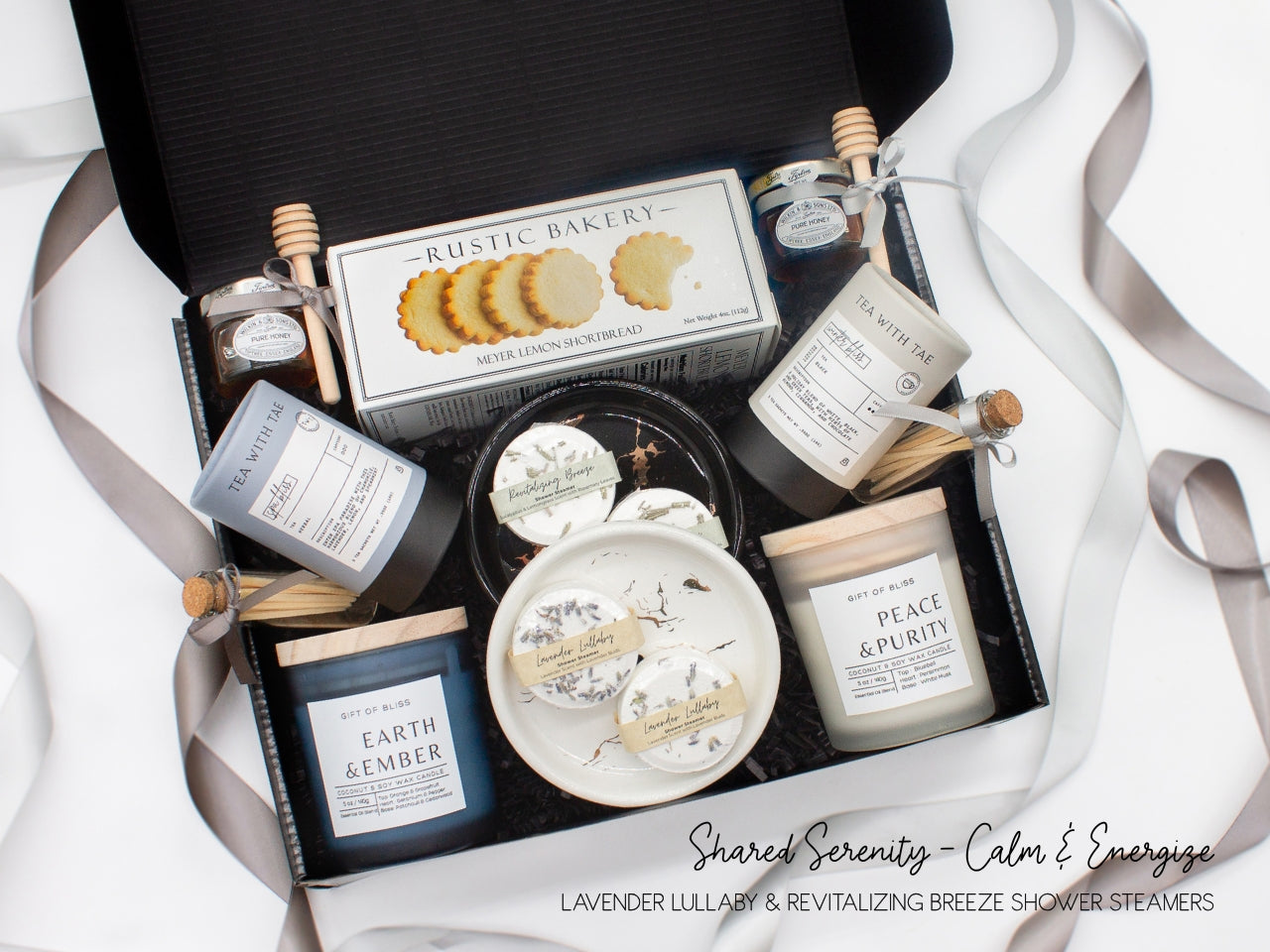A spa gift box for two. Features shortbread cookies, 2 soothing tea blends, honey and wooden dipper, 2 aromatic candles, 2 sets of shower steamers, and 2 sleek ceramic dishes. This elegantly curated box, ideal for couples, enhances shared moments of intimacy and relaxation.