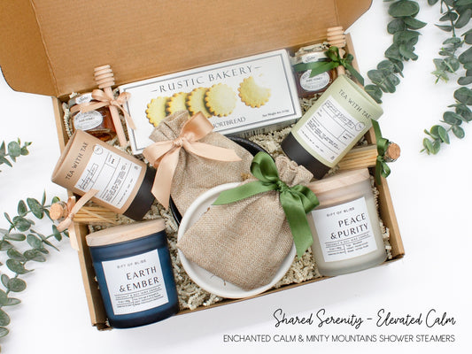 A spa gift box for two. Features shortbread cookies, 2 soothing tea blends, honey and wooden dipper, 2 aromatic candles, 2 sets of shower steamers, and 2 sleek ceramic dishes. This elegantly curated box, ideal for couples, enhances shared moments of intimacy and relaxation.