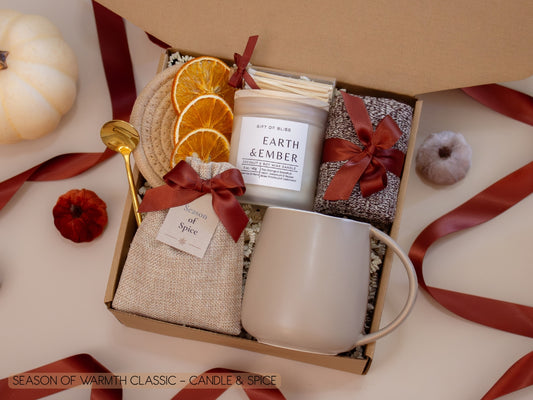 A rustic gift box with a taupe mug, Earth & Ember candle, a burlap sachet of fragrant seasonal spices for mulling or simmering, soft socks, a golden spoon, cinnamon sticks, and dried orange slices—bringing a touch of autumn spice and cozy warmth.