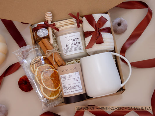 A serene gift box with a taupe ceramic mug, Earth & Ember candle, Bombay Chai tea, honey jar with dipper, California Crisps orange slices, soft socks, and cinnamon sticks—perfect for quiet tea moments filled with gentle warmth.