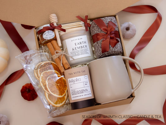 A serene gift box with a taupe ceramic mug, Earth & Ember candle, Bombay Chai tea, honey jar with dipper, California Crisps orange slices, soft socks, and cinnamon sticks—perfect for quiet tea moments filled with gentle warmth.