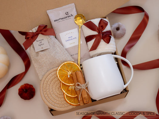 A cozy kraft box with a taupe mug, Moonstruck cocoa bar, burlap sachet of seasonal spices for mulling or simmering, soft socks, golden spoon, cinnamon sticks, and dried orange slices—created to wrap chilly nights in comforting chocolate and spice.