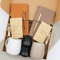 A gift box for two, features two ceramic mugs, two notebooks with a gold pen and a wooden pen, gourmet caramel candies, and two aromatic candles. Perfect for couples, friends, or colleagues to enjoy a relaxing, creative experience together.