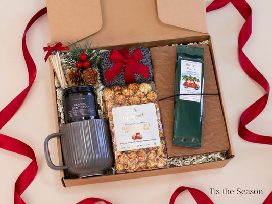 Festive red-and-gray holiday gift box for him featuring a gray ceramic mug, Classic Gentleman candle, caramel popcorn, Butter Rum coffee, cozy socks, pine and berry décor, and a leather-look journal - a warm and cheerful Christmas gift that blends comfort and celebration.