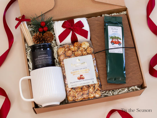 Festive red-and-gray holiday gift box for him featuring a gray ceramic mug, Classic Gentleman candle, caramel popcorn, Butter Rum coffee, cozy socks, pine and berry décor, and a leather-look journal - a warm and cheerful Christmas gift that blends comfort and celebration.