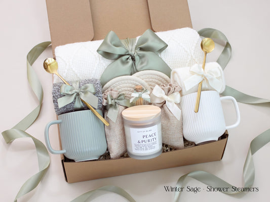 A beautifully curated gift box for couples from the Winter Sage Collection featuring a white knit blanket, two mugs, soft socks, 2 bags of aromatherapy shower steamers, and a Peace & Purity candle. Designed in calming sage and cream hues with an elegant satin ribbon, a thoughtful gift for any occasion.