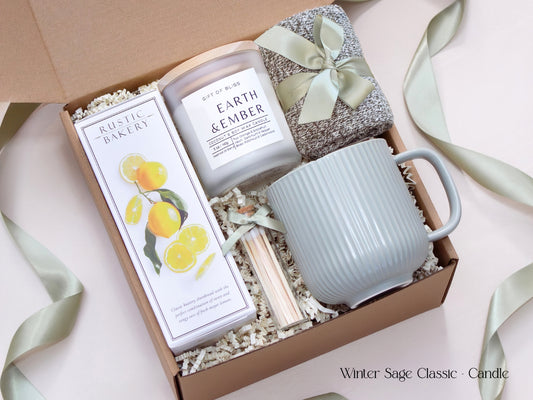 Neutral-toned gift box with a white candle, ribbed sage mug, shortbread cookies, cozy socks, and matches tied with a satin sage ribbon, exuding calm and minimal winter elegance.