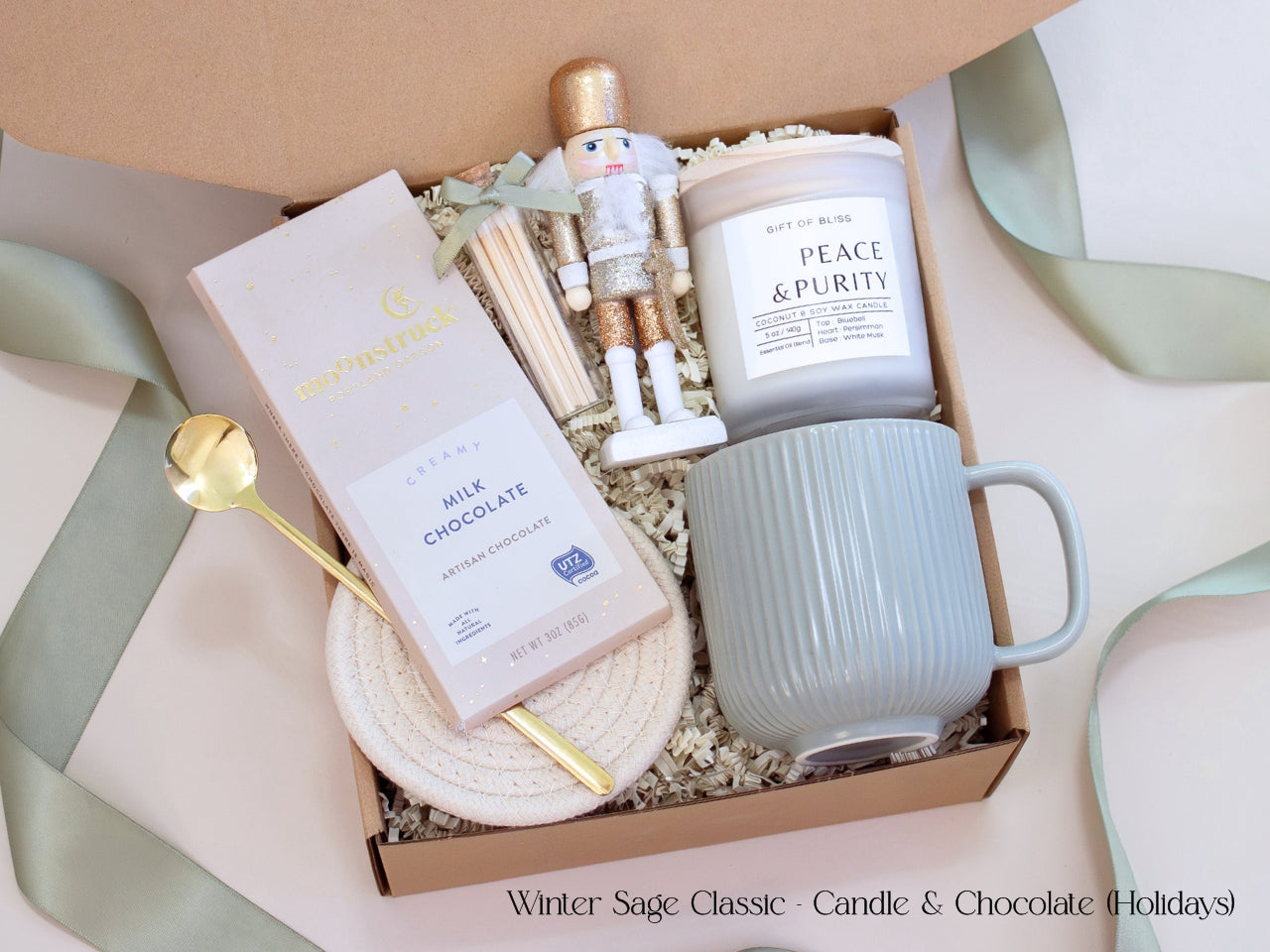 Holiday-themed neutral gift box with a Moonstruck chocolate bar, Earth & Ember candle, sage mug, gold spoon, and nutcracker figurine, styled with sage ribbon and shredded ivory filler for a modern festive touch.