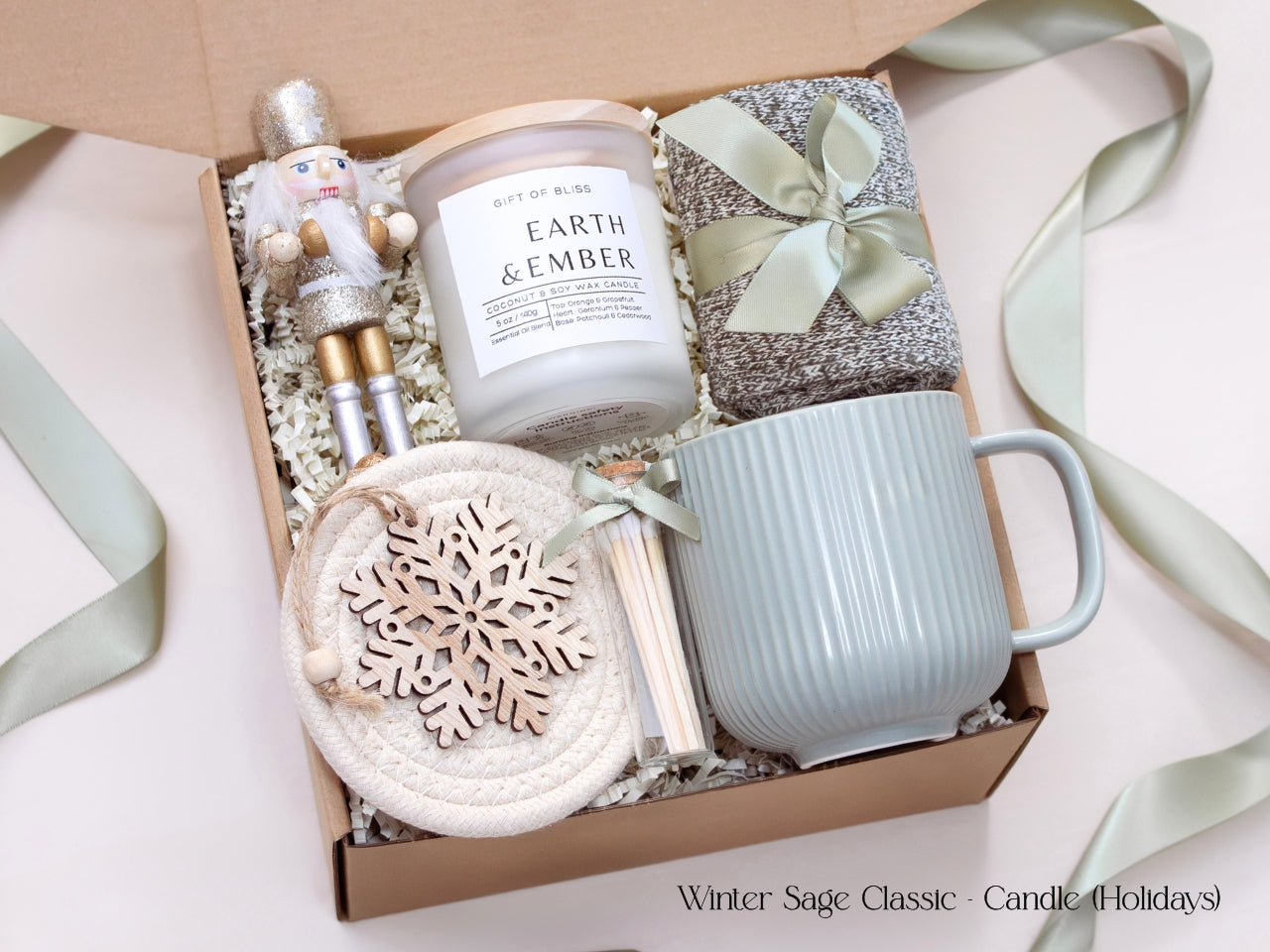 Elegant holiday gift box featuring an Earth & Ember candle, sage mug, cozy socks, matches, and a wooden snowflake ornament, accented with a shimmering nutcracker figure.