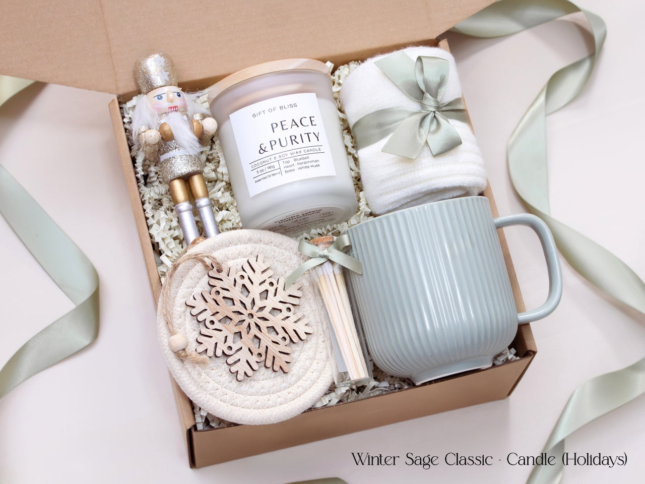 Elegant holiday gift box featuring an Earth & Ember candle, sage mug, cozy socks, matches, and a wooden snowflake ornament, accented with a shimmering nutcracker figure.