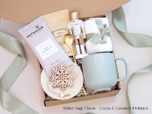 A festive gift box featuring a Moonstruck cocoa packet, caramel candies, nutcracker figurine, sage mug, and wooden snowflake ornament, tied with sage ribbon for a refined winter presentation.
