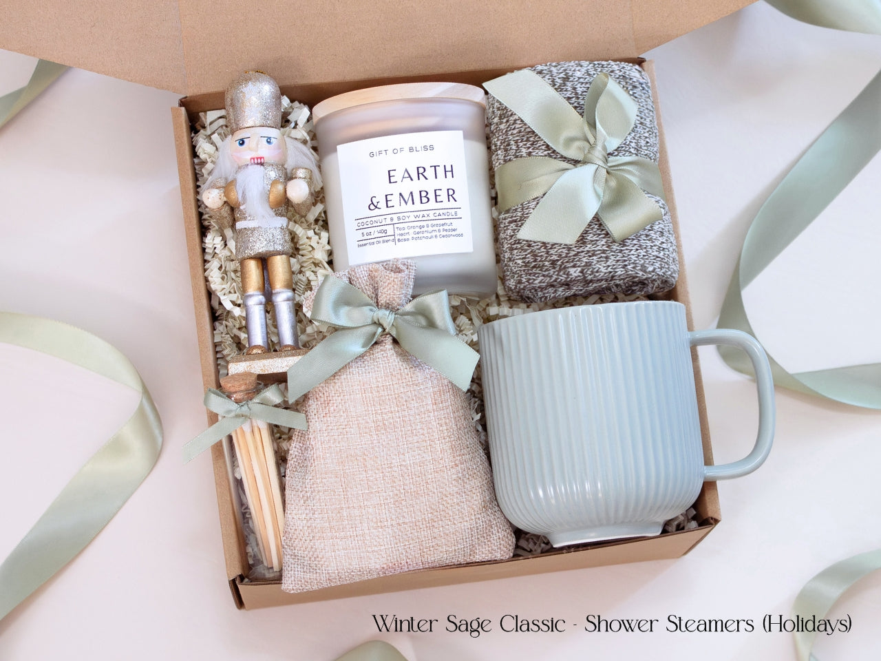 Holiday spa gift box featuring shower steamers in a linen pouch, Earth & Ember candle, ribbed mug, cozy socks, wooden snowflake ornament, and a silver-gold nutcracker accent.