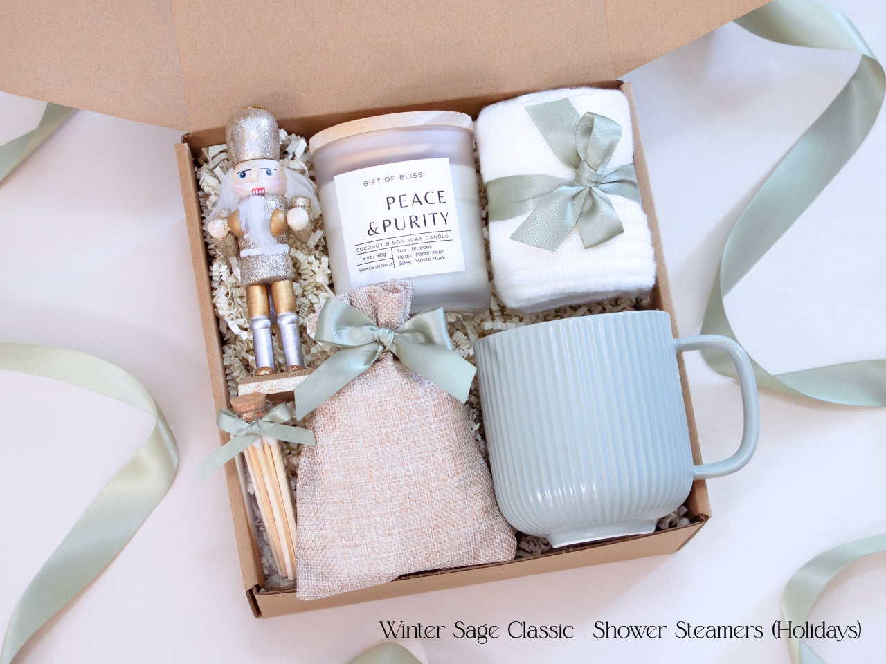 Holiday spa gift box featuring shower steamers in a linen pouch, Earth & Ember candle, ribbed mug, cozy socks, wooden snowflake ornament, and a silver-gold nutcracker accent.